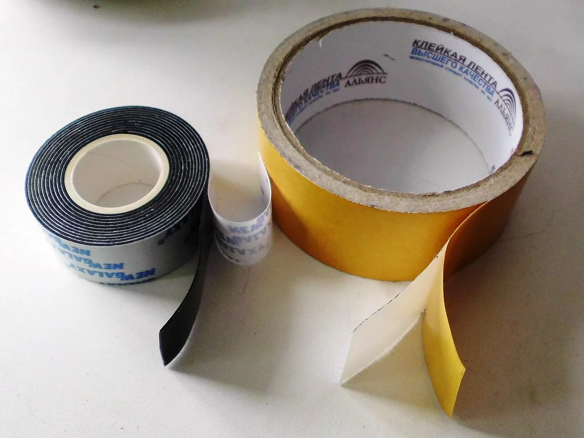 Twee rollen dubbelzijdige tape met wit rugpapier, liggend op een houten ondergrond.