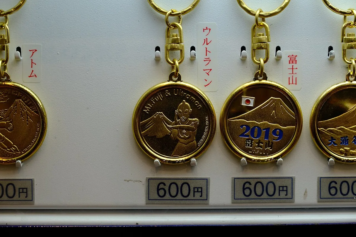 Een souvenirsleutelhanger met een klein gekleurd figuurtje, hangend aan een metalen ring tegen een lichte achtergrond.